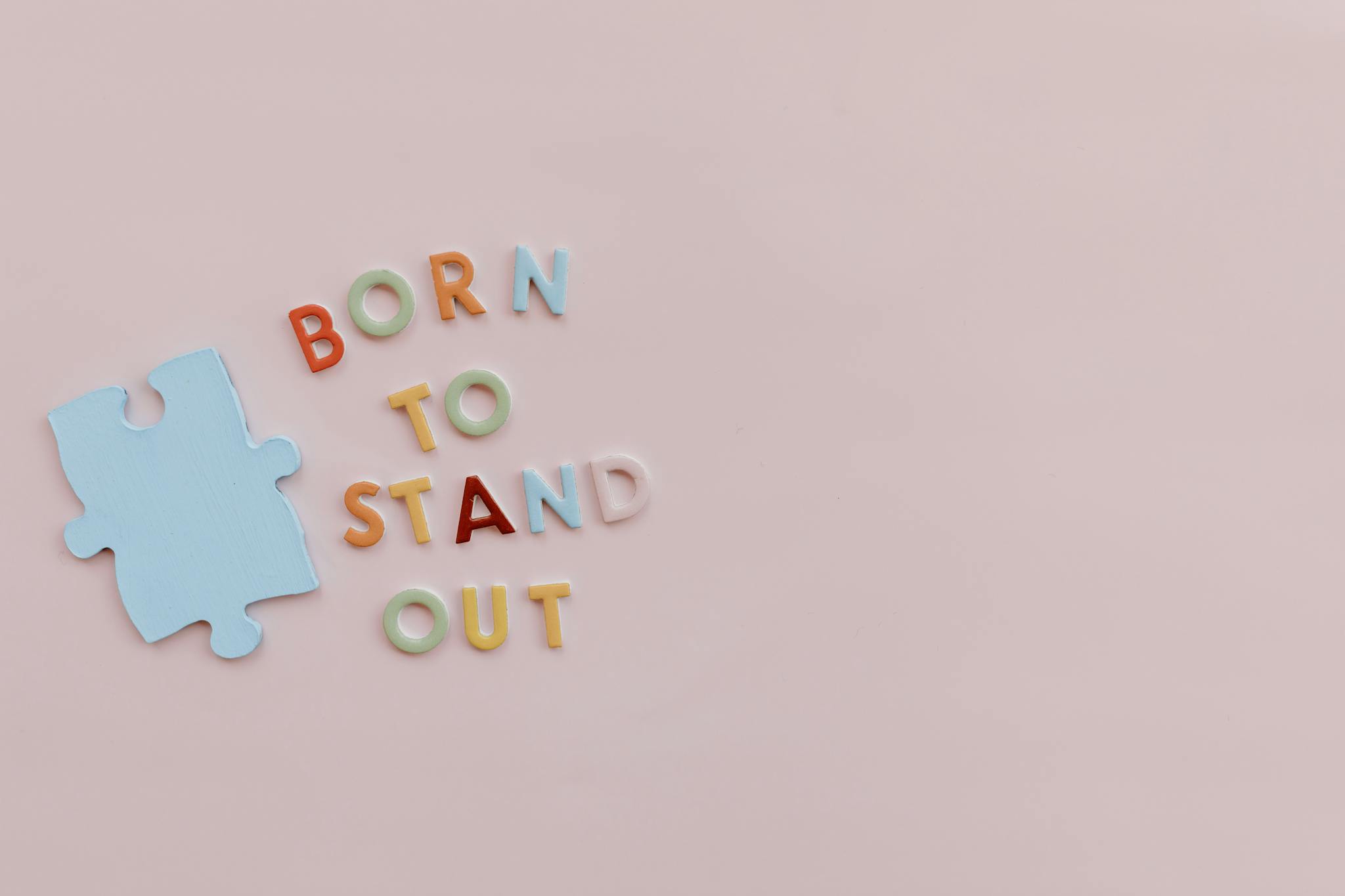Colorful letters spelling 'Born to Stand Out' with puzzle piece symbolizing autism awareness on pink background.